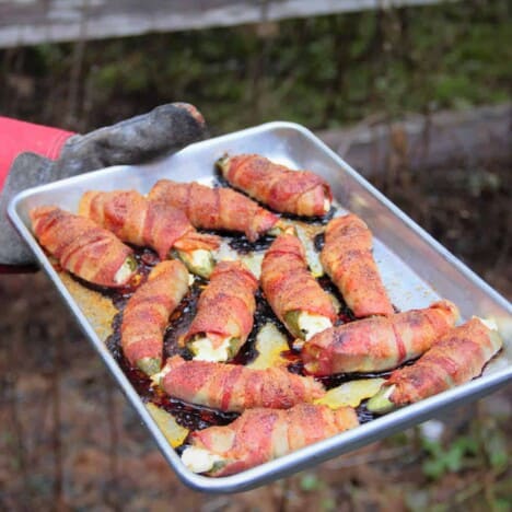 A baking sheet filled with crisp bacon wrapped jalapeno poppers is being held by a person wearing a protective glove.