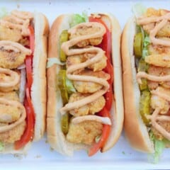 Looking down onto assembled shrimp po'boys with fried shrimp, pickles, tomatoes, and sauce drizzled on top.