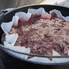 A chocolate cherry cola dump cake in a paper liner in a Dutch oven waiting to be served.