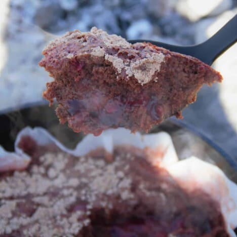 A spoonful of Cheerwine cherry cola dump cake being held above the Dutch oven it was cooked in.