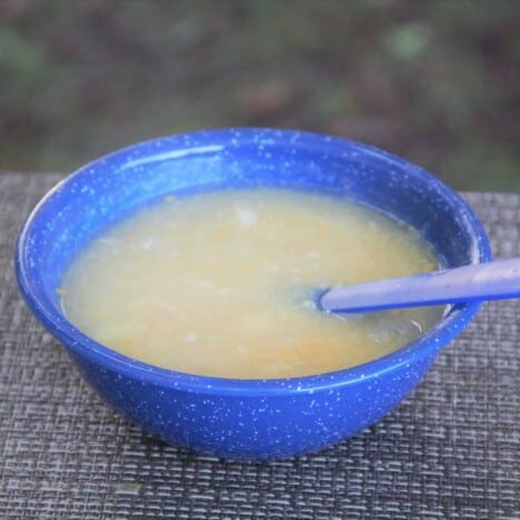 A blue camp bowl filled with a serving of the chicken and corn soup.