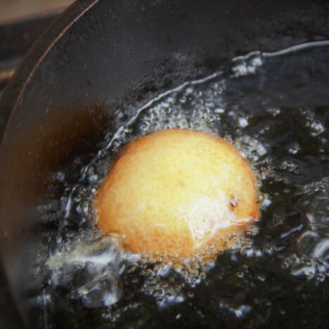 A ball of batter which surrounding an Oreo cooking is deep frying to golden brown in a pot of oil.