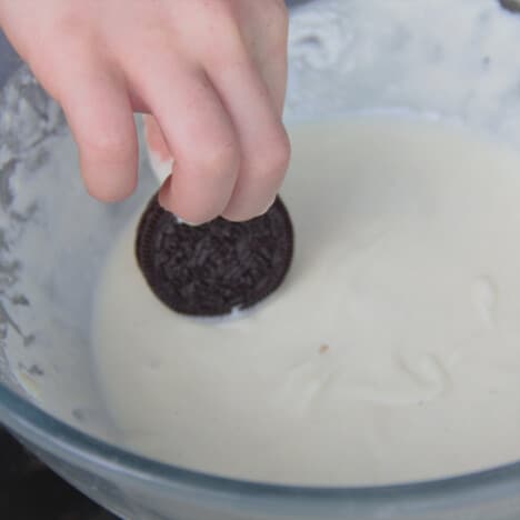 An Oreo being dipped by hand into the bowl of prepared batter.