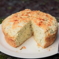 A round loaf of herb and garlic quick bread on a plate with a wedge cut out of it.