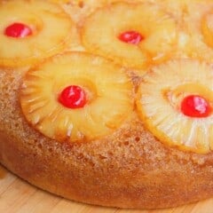 A close up of several pineapple rings with a cherry in the center on a white cake.