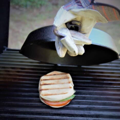 A skillet being lifted from a grilled caprese panini on a grill.