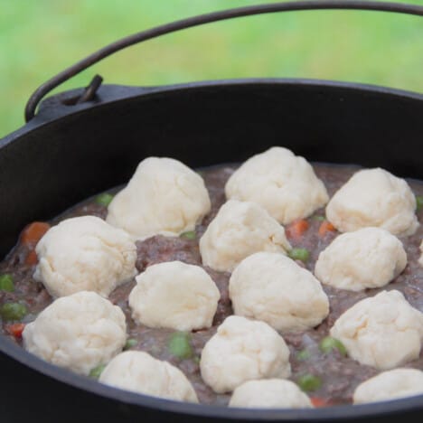 A Dutch oven filled with beef stew and recently added balls of the dumpling dough waiting for the lid added to be cooked.