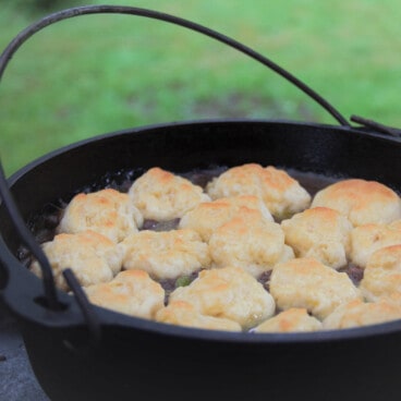 A Dutch oven with the lid removed showing a recently finished minced and dumplings with browned tops.