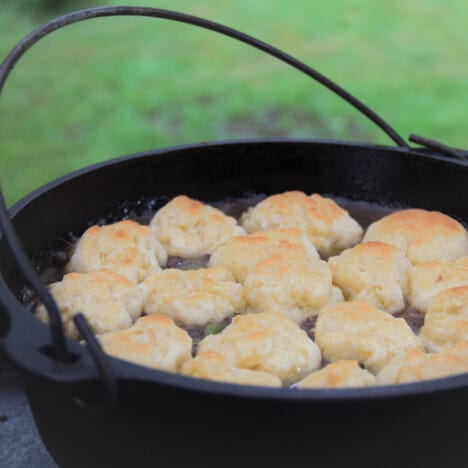 A Dutch oven with the lid removed showing a recently finished minced and dumplings with browned tops.