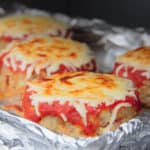 A close up shot of baked mini pizza meatloaves with golden brown melted cheese on a foil-lined baking pan.