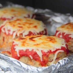 A close up shot of baked mini pizza meatloaves with golden brown melted cheese on a foil-lined baking pan.