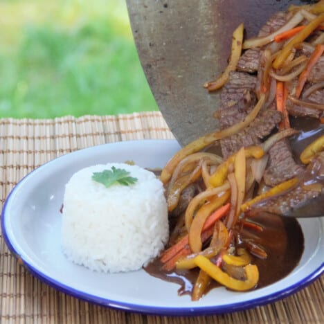 A camp plate with rice on it having the stir fried beef and black bean bean sauce poured on directly from the wok.