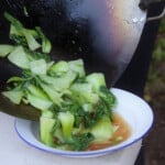 A deep white camp plate is having the stir fried bok choy poured in directly from the wok.