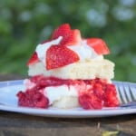 Side view of a stacked strawberry shortcake served on a camp plate with layers of cake, whipped cream, and fresh and canned strawberries.