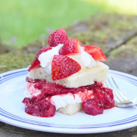A serving of strawberry shortcake using stewed and fresh strawberries sitting on a white and blue camp plate.