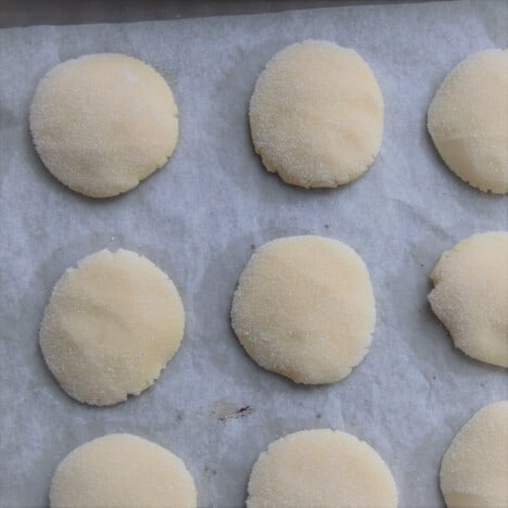 A row of round sugar cookies on a parchment-lined baking sheet.