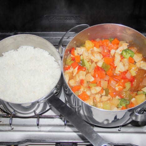 Looking down on a camp stove with a large pot of sweet and sour stew and a small pot of rice.