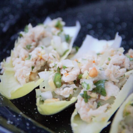 A row of three Belgian endive leaves fill with chicken larb sit on a black camping plate.