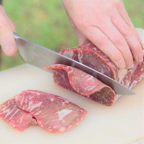 A slab of beef being cut into thin slices for jerky.
