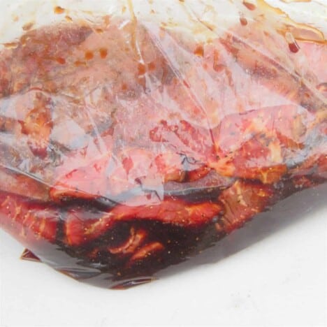 A plastic bag filled with thinly sliced beef surrounded in the dark marinade.