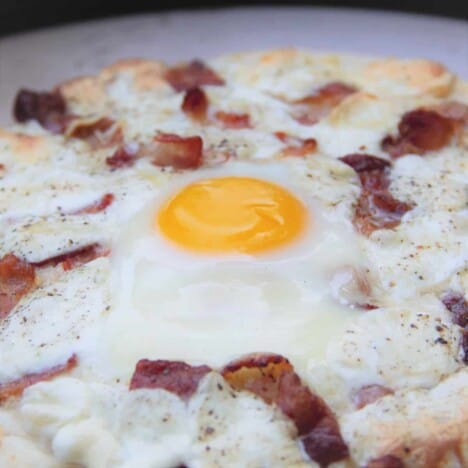 A close-up of the cooked egg on a finished bacon and egg breakfast pizza.