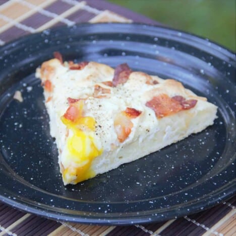 A slice of bacon and egg pizza on a black camp plate.