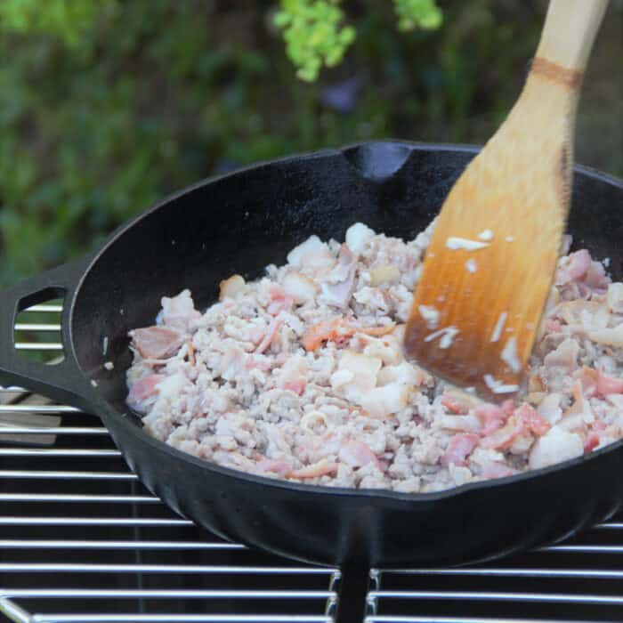 Ground turkey and bacon being sautéed in a skillet over a grill.
