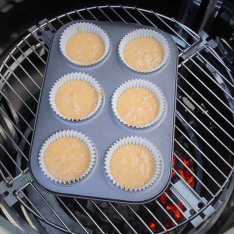 Looking down into a 6-hole muffin tray filled with half baked batter, on a grill in a camping oven.