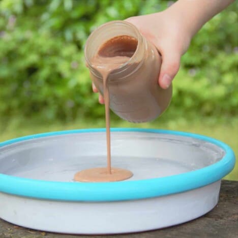A jar of liquid chocolate ice cream base is being poured onto the ice cream block with a light blue rim.