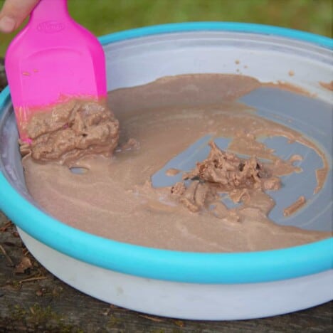 Chocolate ice cream being moved around with a spatula on a stainless ice cream freezing block with a light blue rim.
