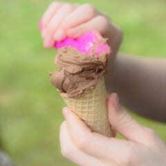 Chocolate ice cream being put into an ice cream cone using a bright pink spatula.