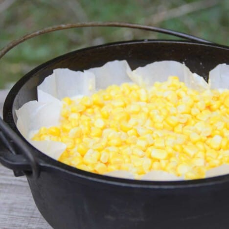 Looking across a Dutch oven filled with a corn dump cake but highlighting the white baking paper and corn kernels on top.