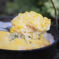 A spoon serving being shown with the creamy corn base, cornbread middle, and kernel top with the full corn dump cake in the background.
