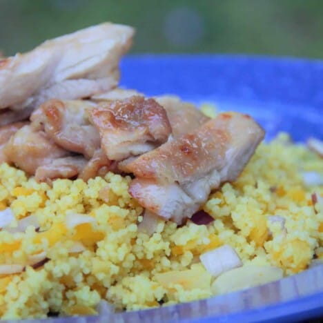 A blue camp plate with a bed of apricot couscous is topped with sliced glazed chicken thighs