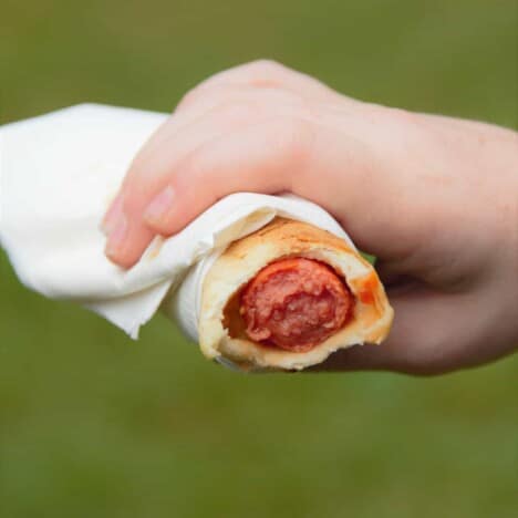A campfire hot dog wrap with a bite out of it being held in a white paper napkin.