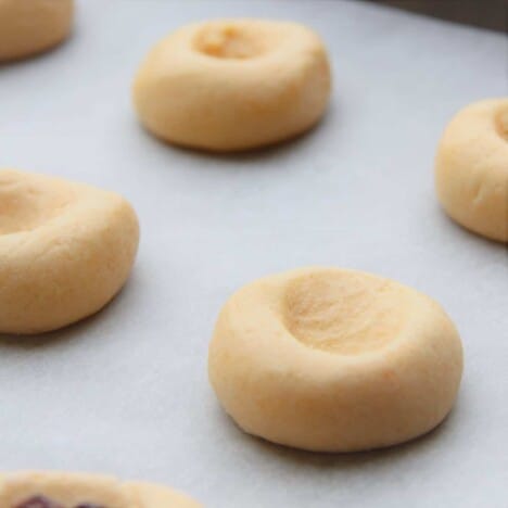 A paper lined baking tray with the cookie dough with thumb prints in them.