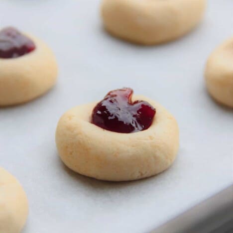 Close up of a raw cookie with a thumbprint filled with raspberry jam.