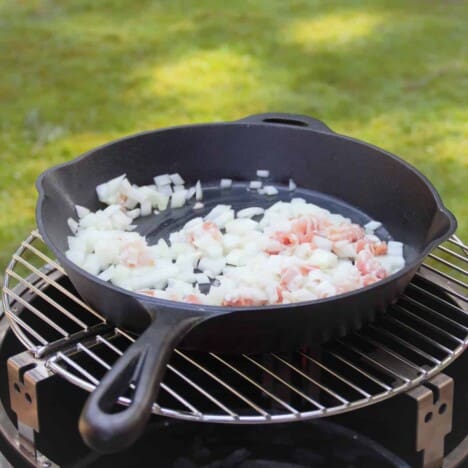 A skillet sitting on an Aquaforno sautéing bacon and onions.