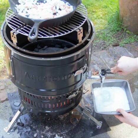 The Aquaforno barbecue with bacon and onions cooking in a skillet on the top while water from the bottom is being added to a tray of dehydrated mashed potatoes.