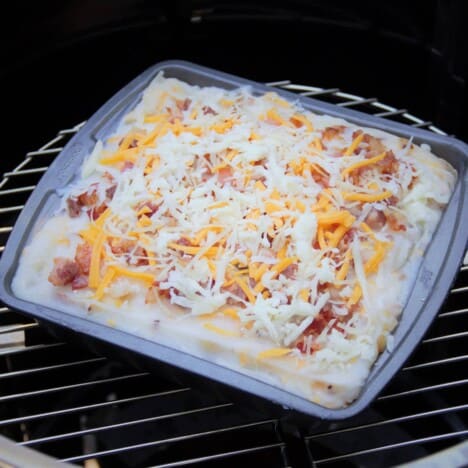 A square baking pan filled with mashed potatoes and sprinkled with cheese sits in a camp oven.