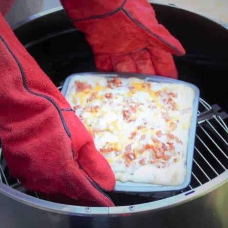 A square baking pan of loaded mashed potatoes being removed from the Aquoforno which was being used as a camp oven.