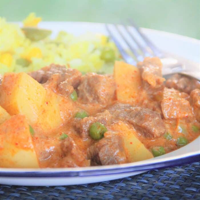 A close up shot of beef Massaman curry with large chunks of potatoes and pops of peas in a rich brown gravy.