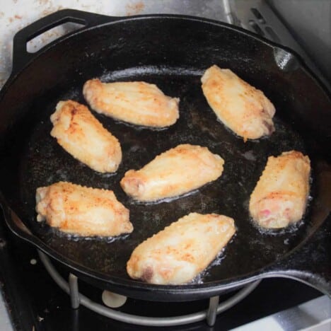 A skillet on a camp stove frying flour dusted chicken wings.