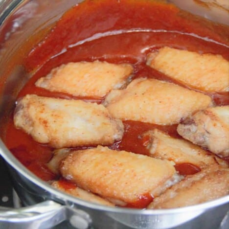 A pot of buffalo sauce with cooked chicken wings in it waiting to be stirred through.