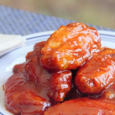 A served plate of chicken wings covered in a bright and glossy red buffalo sauce.
