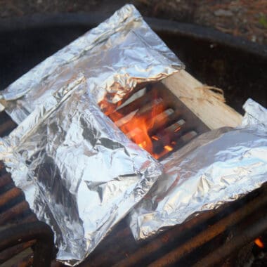 Looking down on three rolled up foil packets sitting on a hot grill.