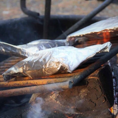Looking across a hot grill with three foil packets sitting on top.