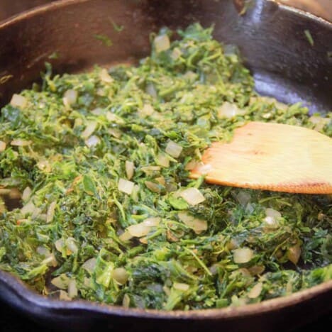 A skillet filled with bright green spinach speckled with white onion.