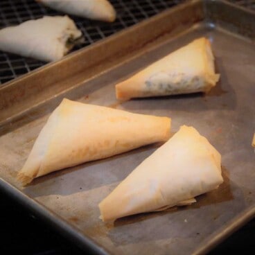 A baking tray with three golden brown cooked spinach and feta triangles.