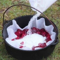 A Dutch oven lined with baking paper and an even layer of strawberry pie filling on the bottom is having a packet of cake mix pour in.